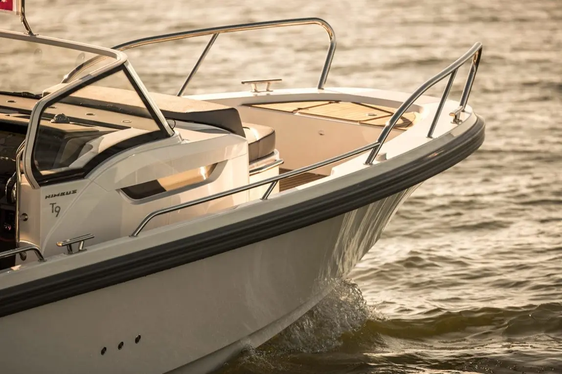 Close-up of a Nimbus T9 boat bow, showcasing sleek design and metal railings against a shimmering water backdrop.